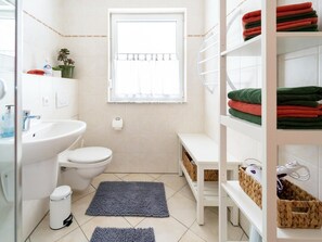 Casa de banho com sanita, lavatório e prateleiras com toalhas dobradas.