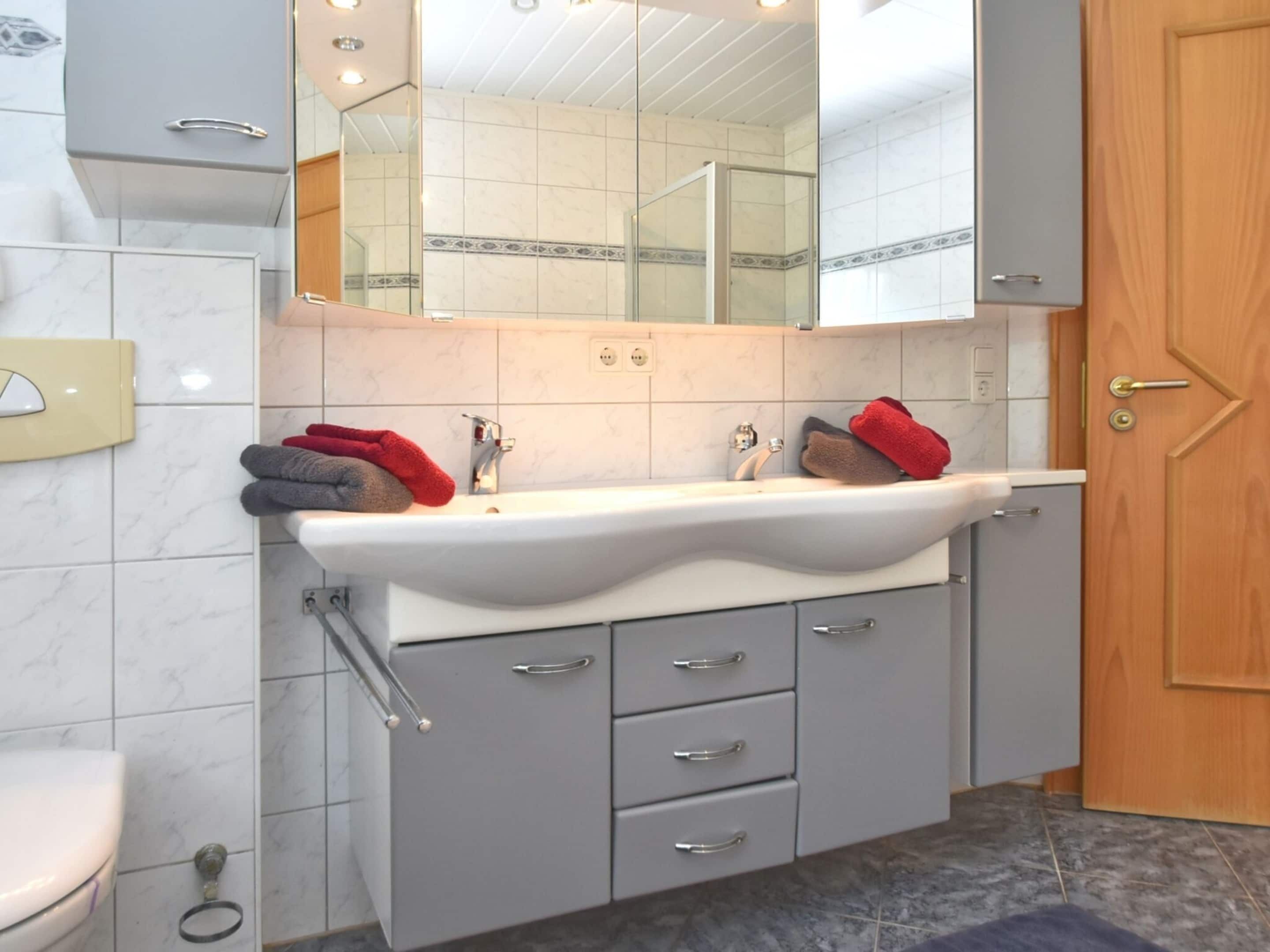Un baño con un lavabo blanco, dos toalleros, un espejo y armarios grises.