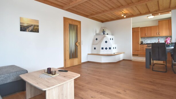 A spacious living area with a wooden ceiling, a dining table, a sofa, and a kitchen in the background. - Apartment in the Bavarian Forest (Zenting)