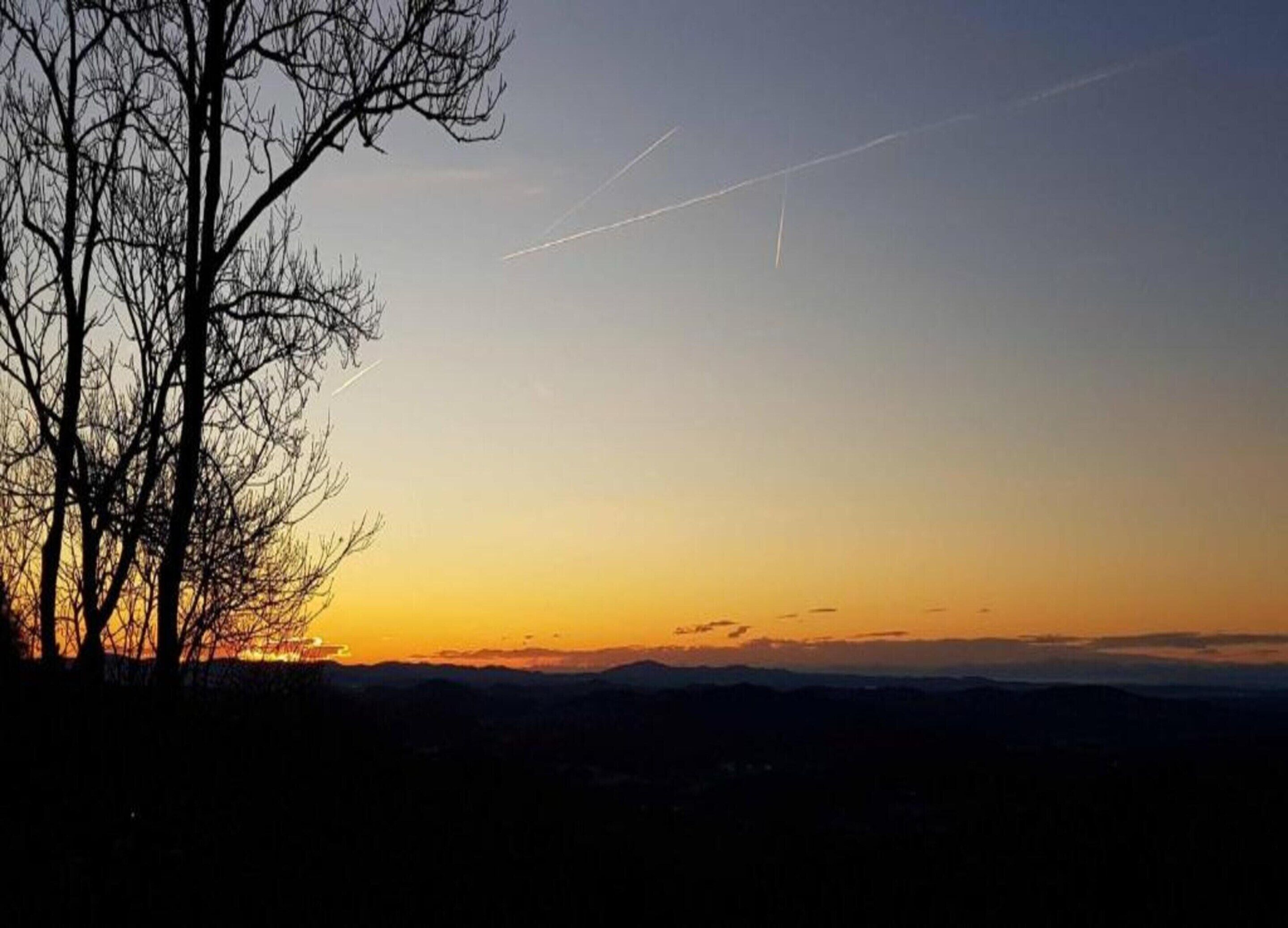 A sunset with a silhouette of a leafless tree and distant mountains.