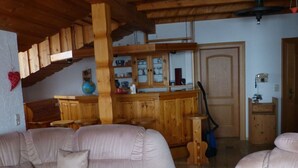 Una sala de estar acogedora con una escalera de madera, una zona de cocina con armarios de madera y una barra.
