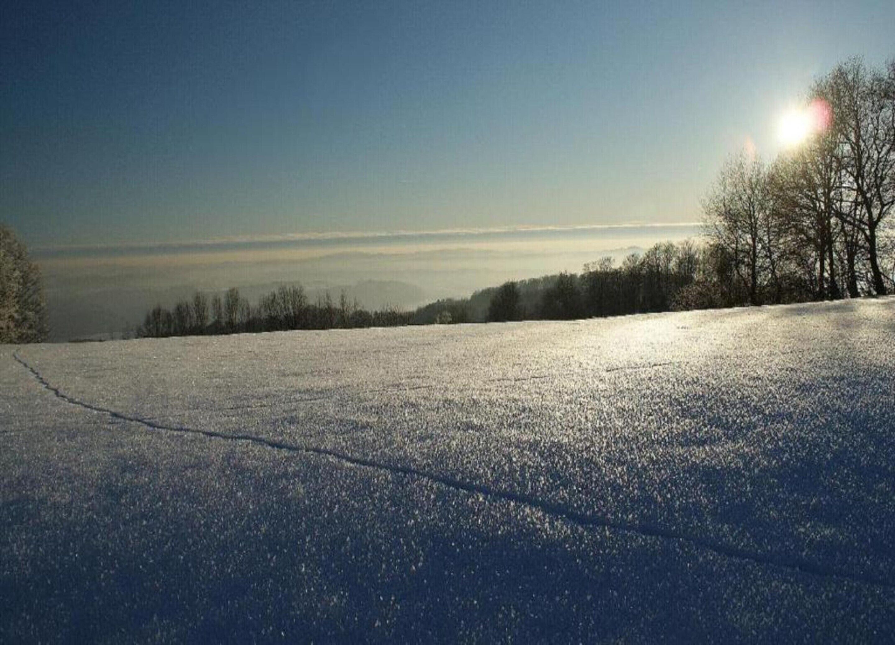 Un paysage enneigé, avec un ciel dégagé et un soleil éclatant.