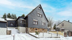 Et toetagers hus med stensokkel og mørk tagsten, omgivet af sne.