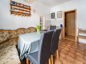 A dining area with a table, chairs, a bench, and a wall-mounted shelf with kitchenware. - Holiday Home With Terrace and Garden (Grossbreitenbach)