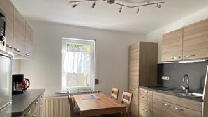 A modern kitchen with wooden cabinets, a dining table with chairs, a coffee maker, and a window with curtains. - Wohnung Nahe Inselsberg Wanderwege (Waltershausen)