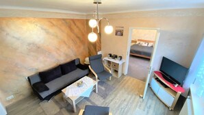 A compact living space with a sofa, a small table, a chair, a TV, and a bed in the background. - Wohnung Nahe Inselsberg Wanderwege (Waltershausen)