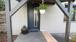 A modern entrance with a dark door, a hanging planter with flowers, and a potted plant on the ground. - Wohnung Nahe Inselsberg Wanderwege (Waltershausen)