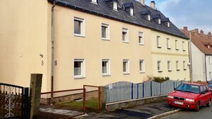 A two-story residential building with a beige facade, multiple windows, and a sloped roof. - Apartment in the Fichtelgebirge (Arzberg)