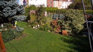 A garden with various plants and flowers, a wooden bench, and a small brick structure. - Apartment in the Fichtelgebirge (Arzberg)