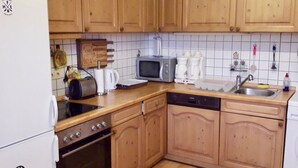 A compact kitchen with wooden cabinets, a microwave, a coffee maker, and a dishwasher. - Apartment in the Fichtelgebirge (Arzberg)