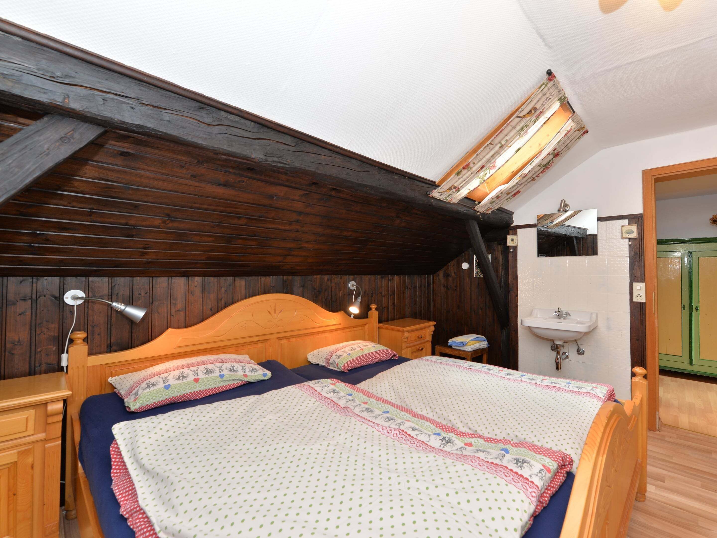 Une chambre avec un plafond en bois, un lit avec une literie à motifs, une table de chevet et une commode.