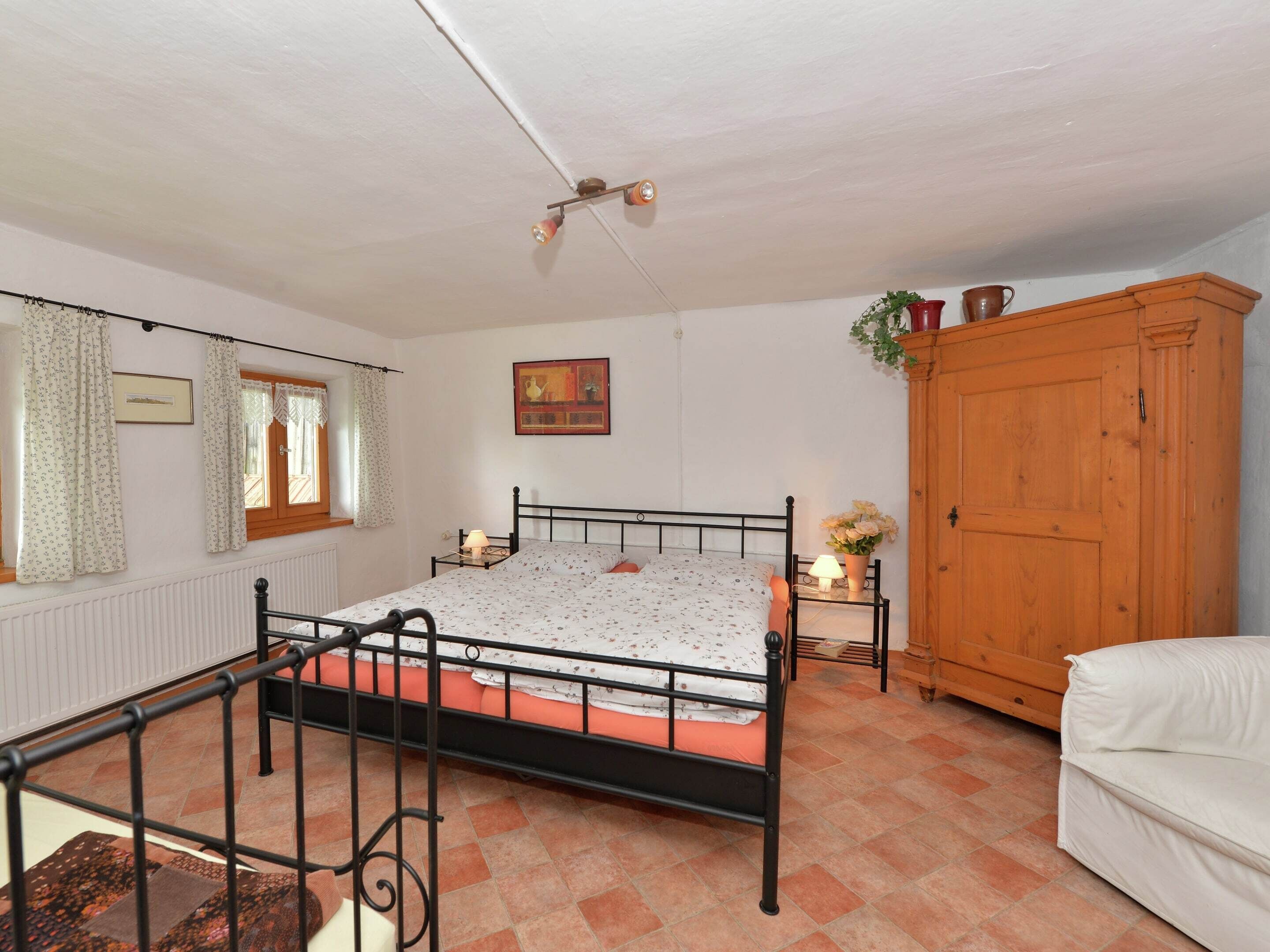 Une chambre à coucher comprenant un lit, une armoire en bois, une fenêtre avec des rideaux, un radiateur et un luminaire au plafond.