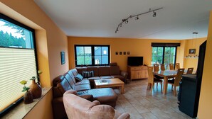 A living room with a sofa, coffee table, TV, and dining area with chairs and a table. - Forest Escape With Terrace (Eisfeld)