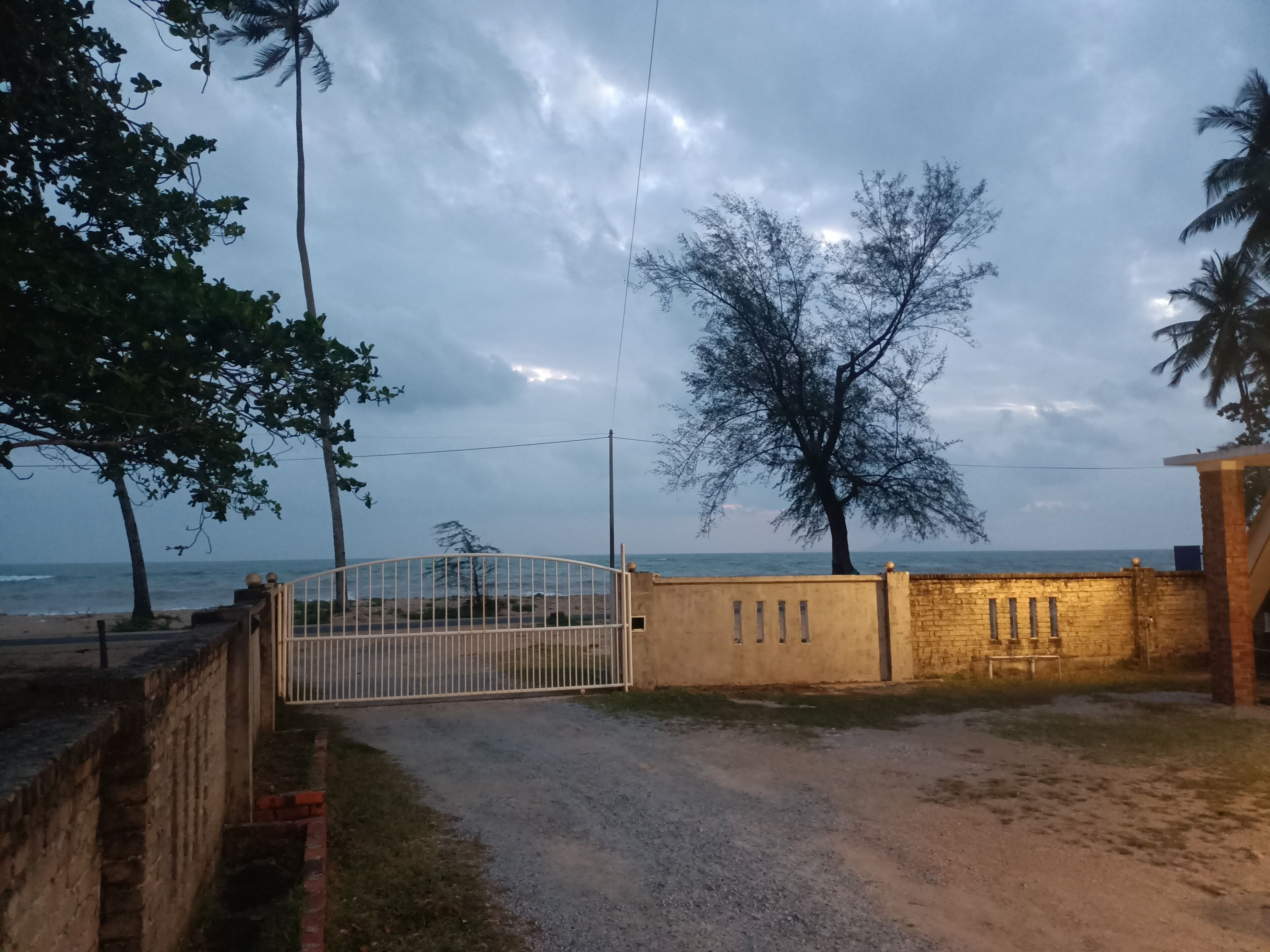 Une entrée fermée par un portail en métal, un mur de briques et une vue sur la mer.