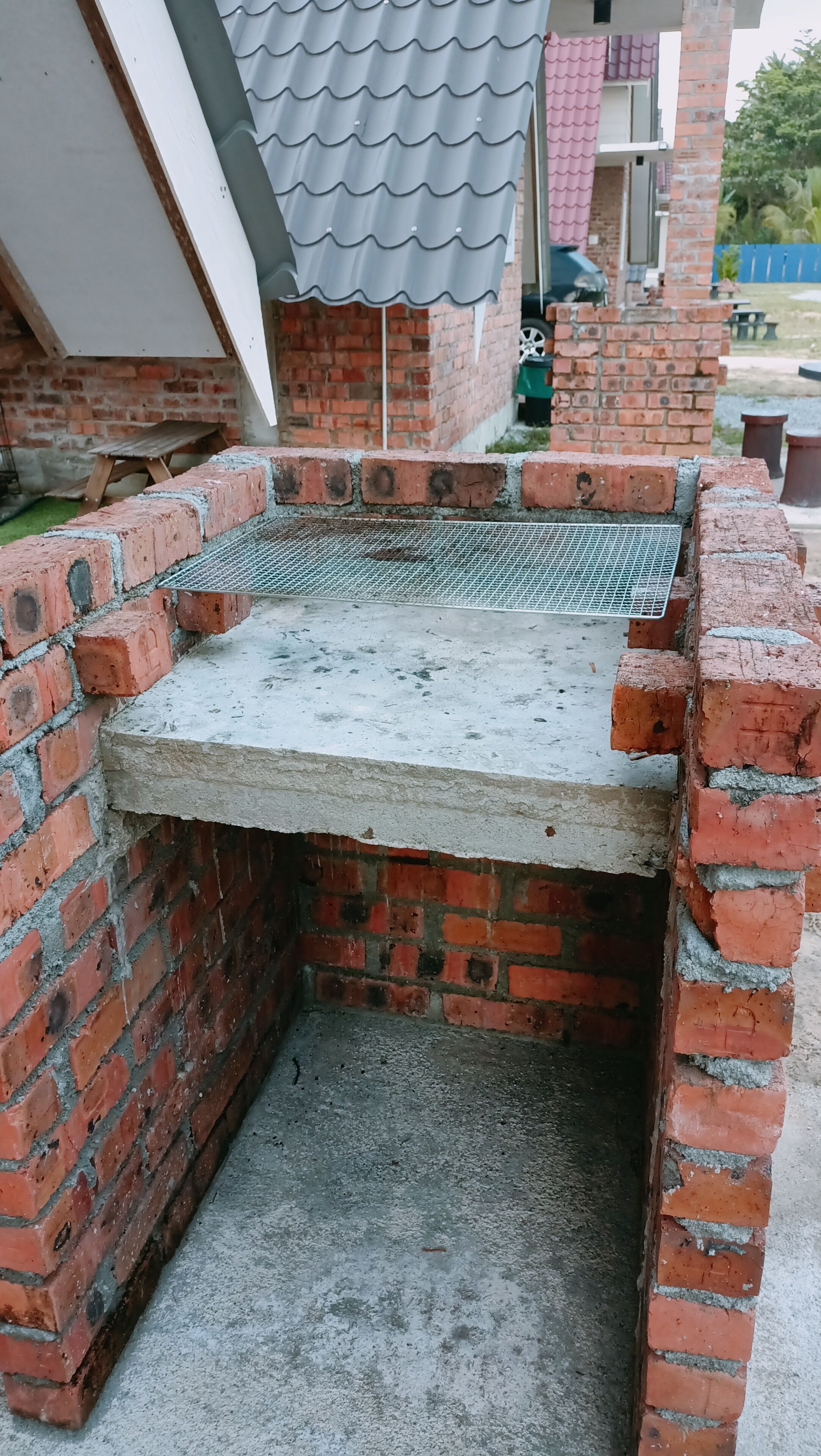 A brick-built outdoor barbecue area with a metal grill and a concrete countertop.