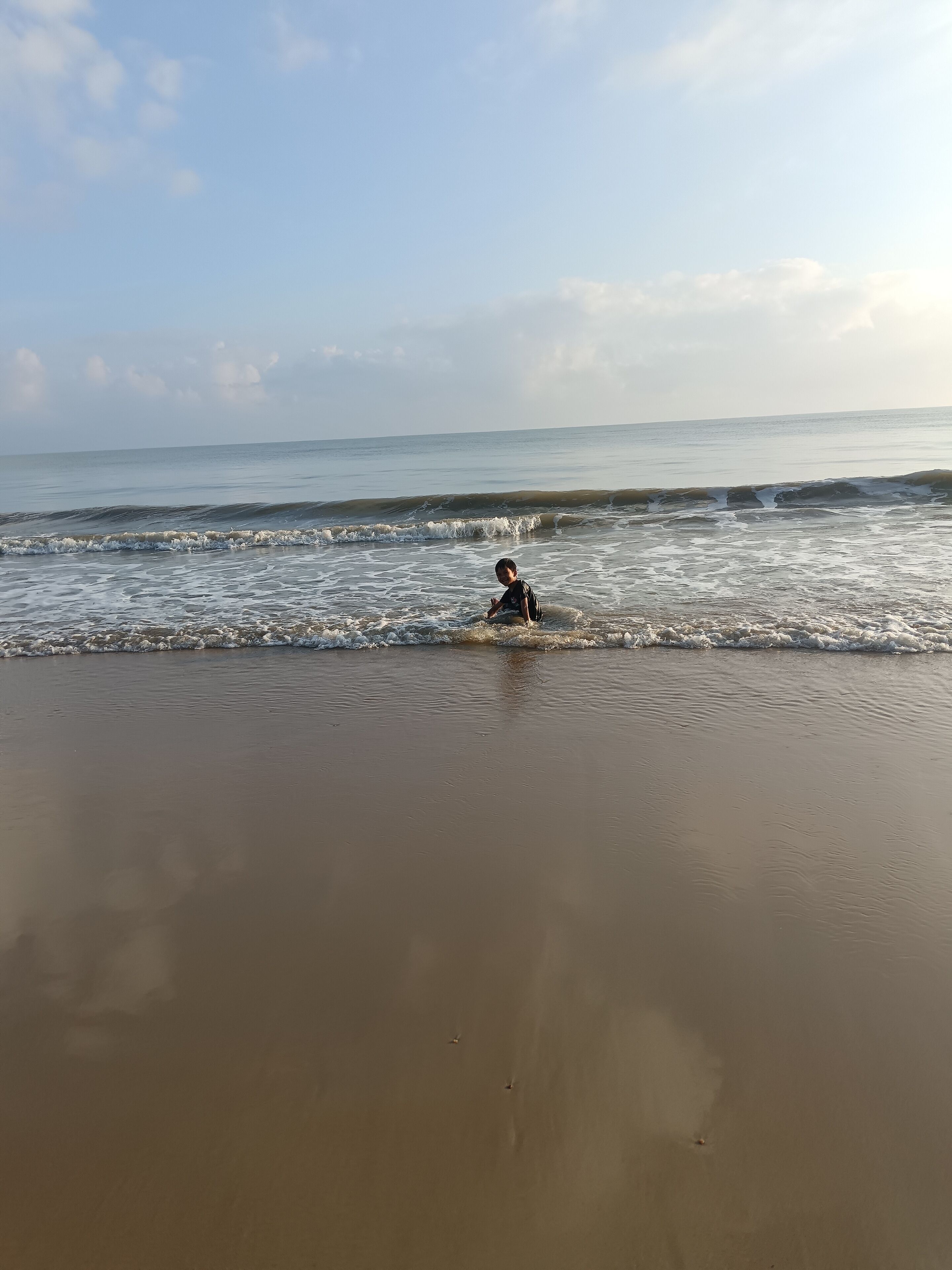 A beach scene with a child playing in the water.