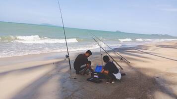 A beach with two people fishing, a fishing rod, and a blue tackle box.