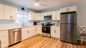 A modern kitchen with white cabinets, stainless steel appliances, and a wooden floor. - 7 Dove Street - 3 Bedroom, newly remodeled home on North Forest Beach (Hilton Head Island)