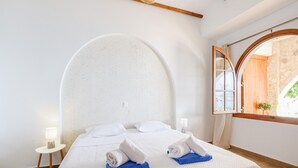 A hotel room with a large bed, a small bedside table with a lamp, and a window with a view of greenery.