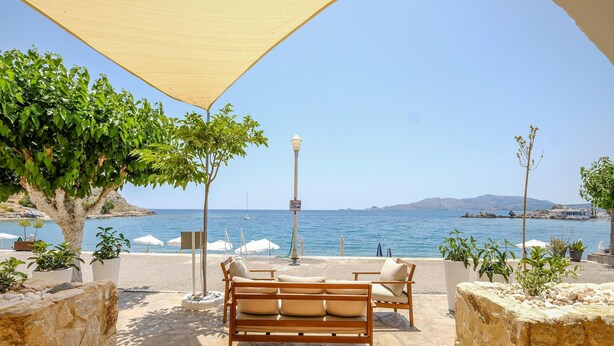 A patio with a wooden bench and potted plants, overlooking a body of water and a distant mountain range.