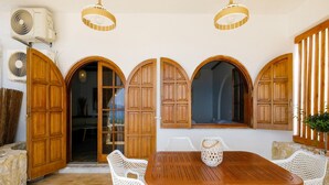 A dining area with a wooden table and white chairs, surrounded by arched wooden doors and windows.