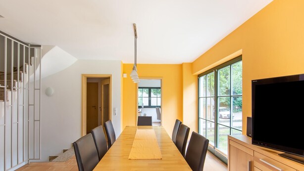 A modern dining area with a long wooden table, black chairs, and a large TV on a wooden cabinet. - Pet-friendly Getaway (Eisfeld)