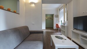Een moderne woonkamer met een grijze bank, een witte salontafel en een flatscreen televisie op een witte standaard.