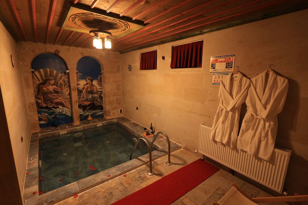 A spa room with a stone bathtub, a red carpet, and two white robes hanging on a radiator.