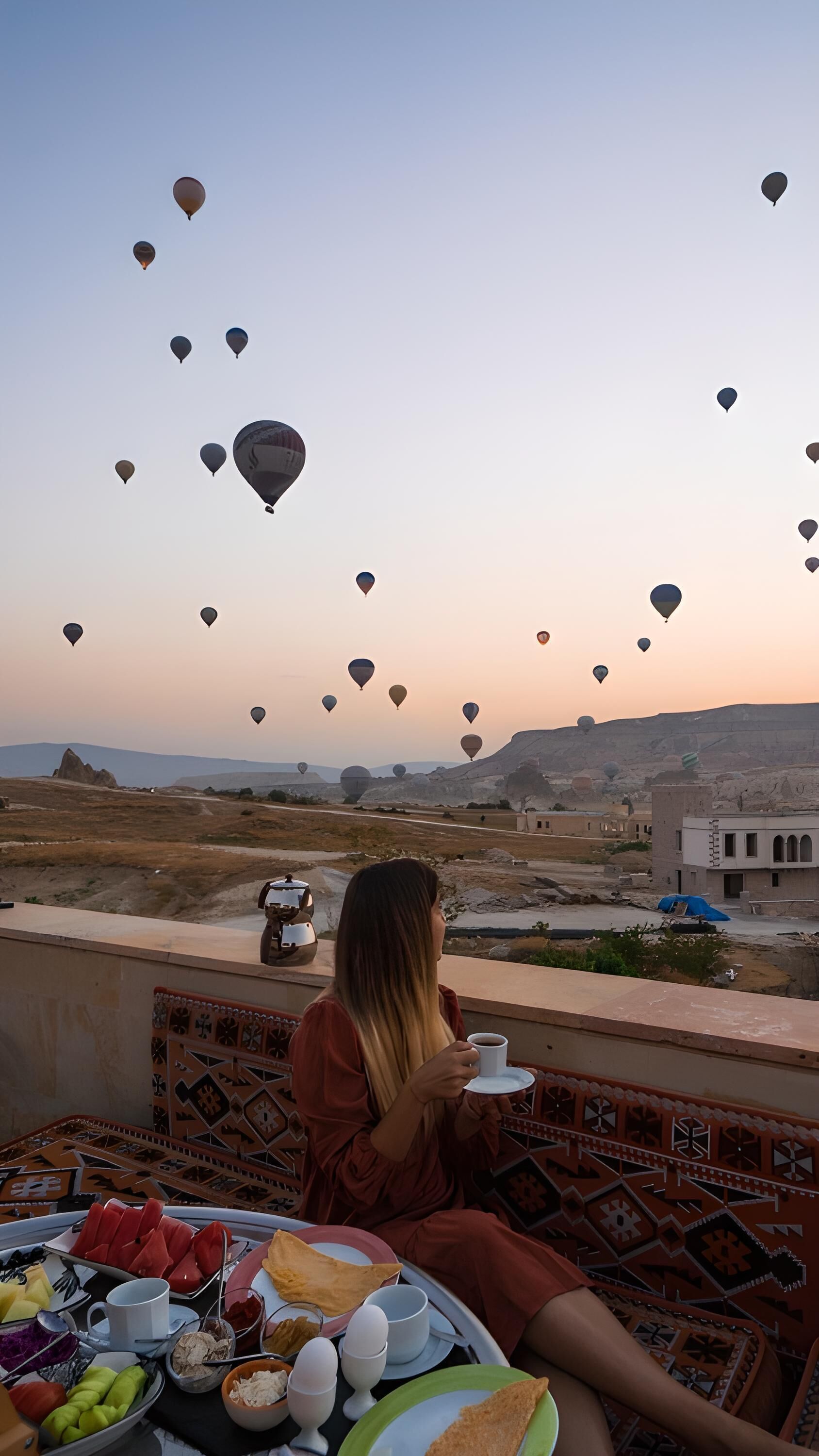 A person enjoying a meal with a view of hot air balloons and a desert landscape.