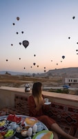 Una persona disfrutando de una comida con vistas a globos aerostáticos y un paisaje desértico.