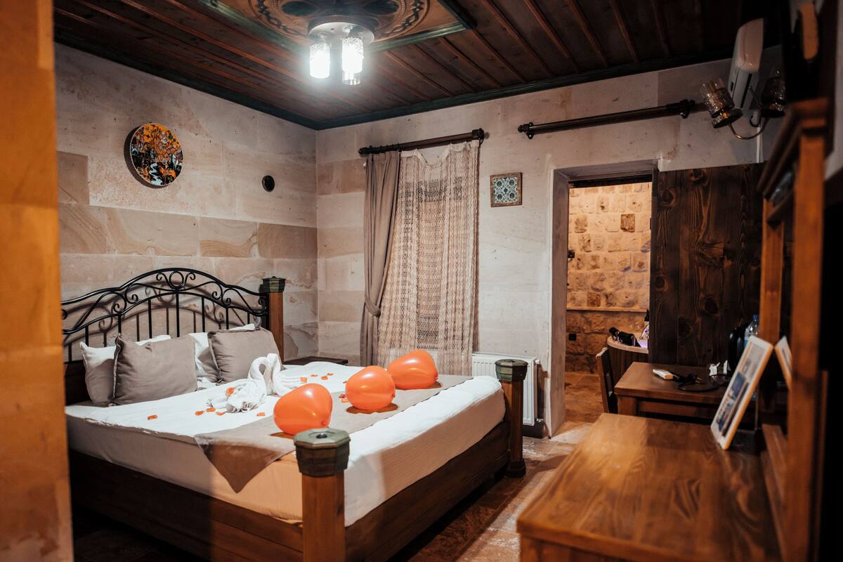 A cozy room with a bed, a wooden table, and a stone wall.
