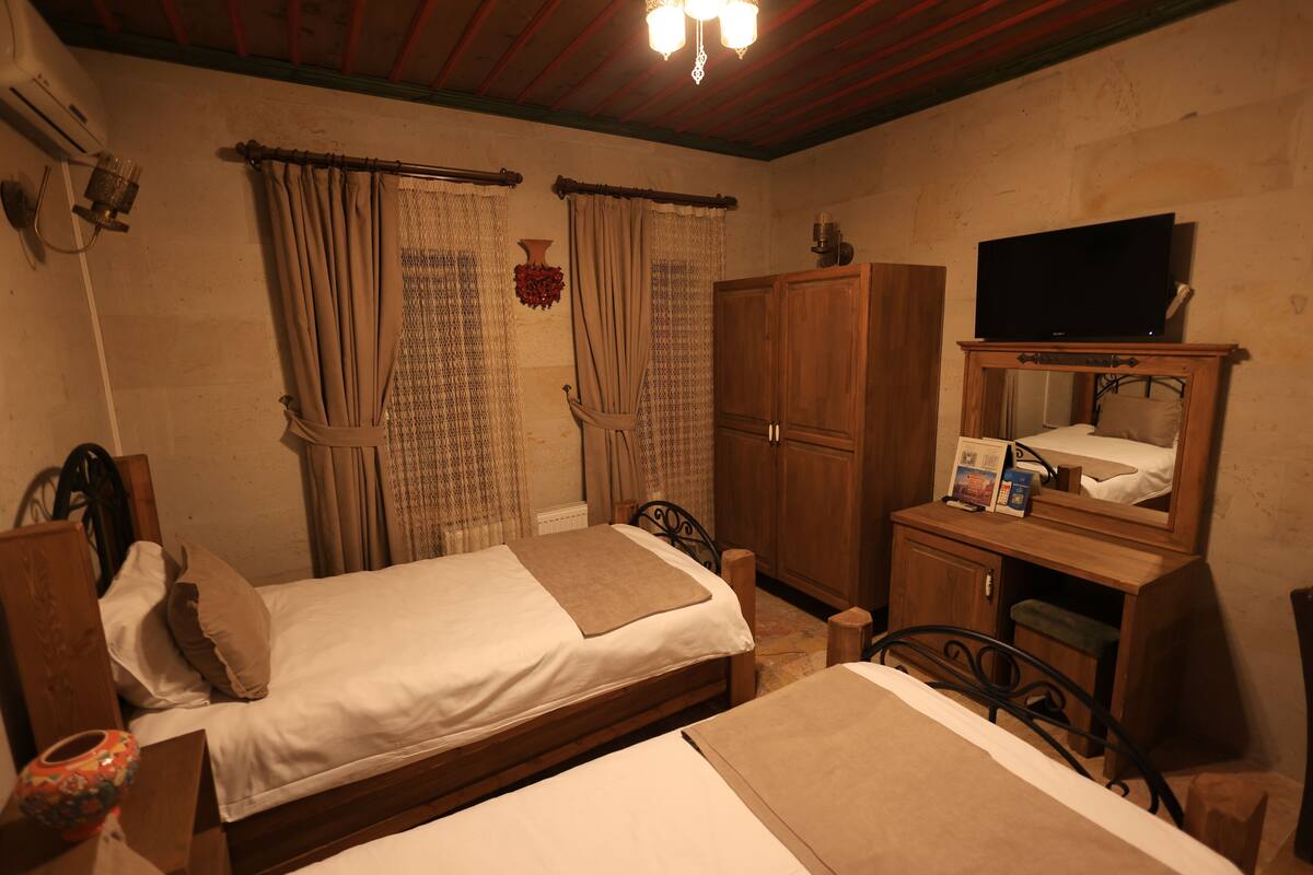 A room with two single beds, a wooden wardrobe, a small desk with a mirror, and a television on a wooden stand.