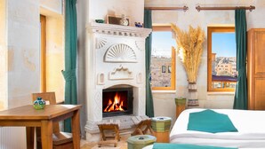 A hotel room with a fireplace, a bed, a table, and a view of the city. - Katapa Stone House (Nevsehir)