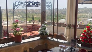 A dining table set with various dishes and drinks, surrounded by large windows with a view of a mountainous landscape. - Katapa Stone House (Nevsehir)