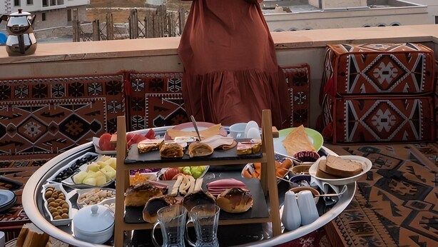 A woman enjoying a meal on a rooftop terrace with a view of hot air balloons and a mountainous landscape. - Katapa Stone House (Nevsehir)