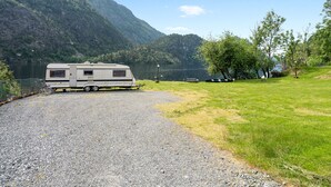 Un espace de stationnement aménagé avec du gravier, où est garé un camping-car près d’un lac, le tout entouré de zones herbeuses et d’arbres.