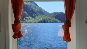 Une fenêtre avec des rideaux orange, une vue sur un lac et un paysage montagneux.