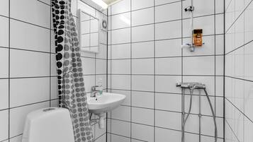 Un baño con paredes de azulejos blancos, un lavabo blanco, un inodoro y una ducha con cabezal de ducha manual.