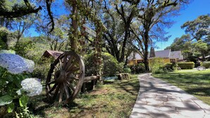 A garden with a wooden wagon wheel, a pathway, and a building with a yellow facade. - Pousada Lago Azul  (Camanducaia)