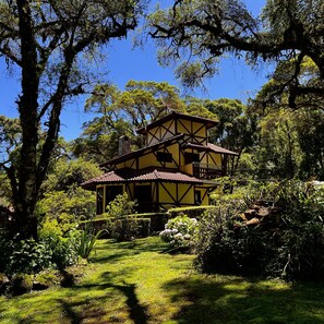 A traditional two-story house with a yellow facade and dark brown trim, surrounded by lush greenery and trees. - Pousada Lago Azul  (Camanducaia)