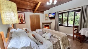 A bedroom with a bed, a fireplace, a TV, and a window with curtains. - Pousada Lago Azul  (Camanducaia)