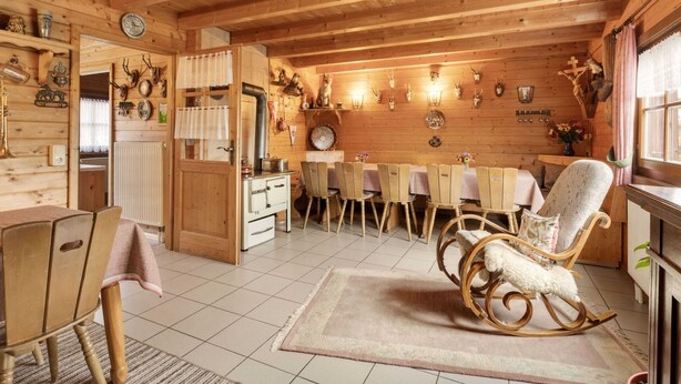 A cozy wooden cabin with a dining area, a kitchen with a stove, and a rocking chair. - Holzferienhaus in Hinterrod mit Sauna (Eisfeld)