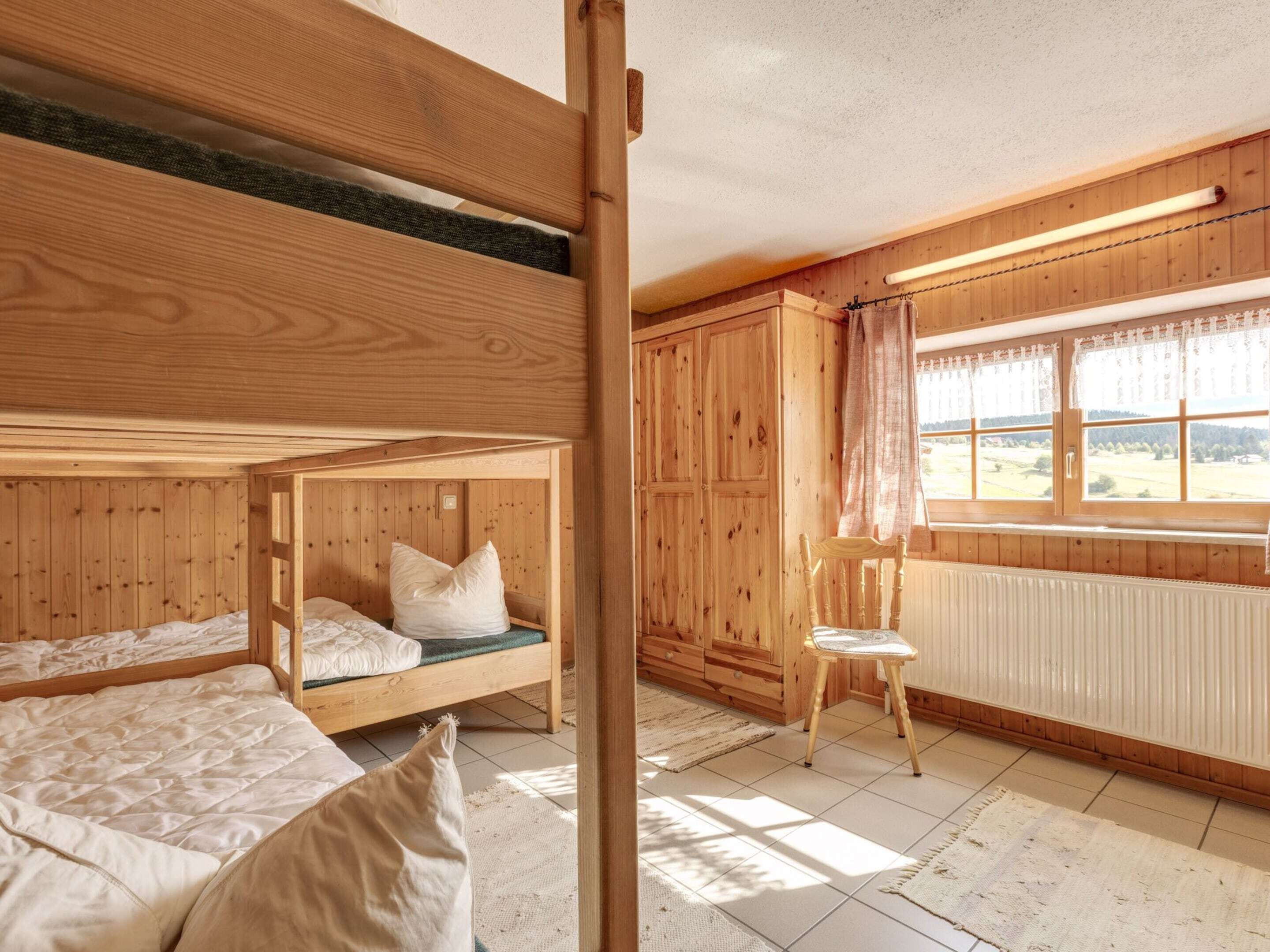 A wooden cabin with bunk beds, a wooden chair, and a window with curtains.