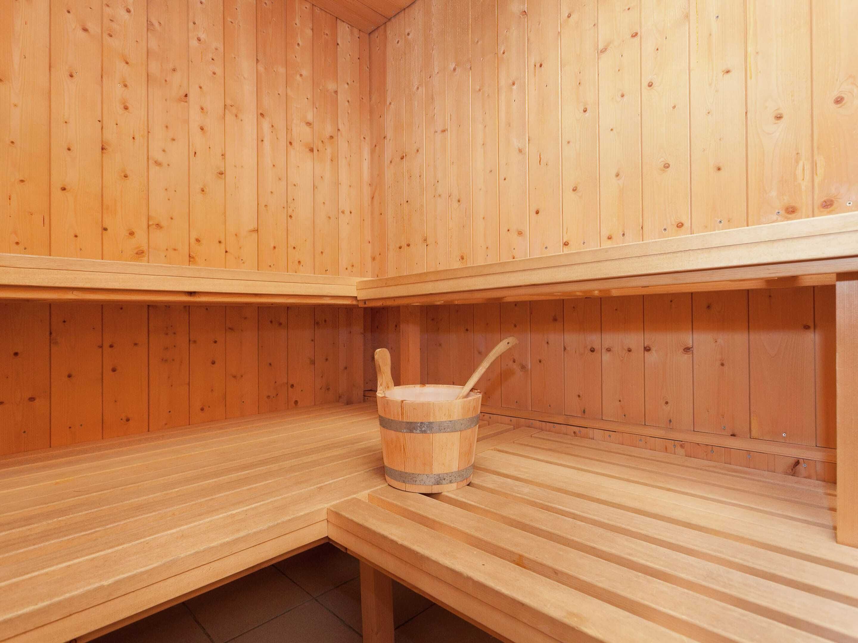 Una sala de sauna con bancos de madera y un cubo de madera con una cuchara.