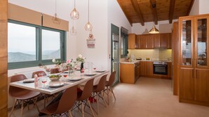 Une cuisine moderne avec des meubles en bois, un coin repas avec une table dressée pour quatre personnes, et une vue sur les montagnes par une grande fenêtre.