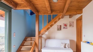Une pièce avec un escalier en bois, un canapé blanc et une vue sur l’extérieur, visible à travers une porte vitrée.