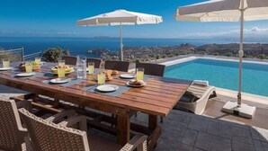 Une table à manger avec des parasols, une piscine et une vue sur l’océan.