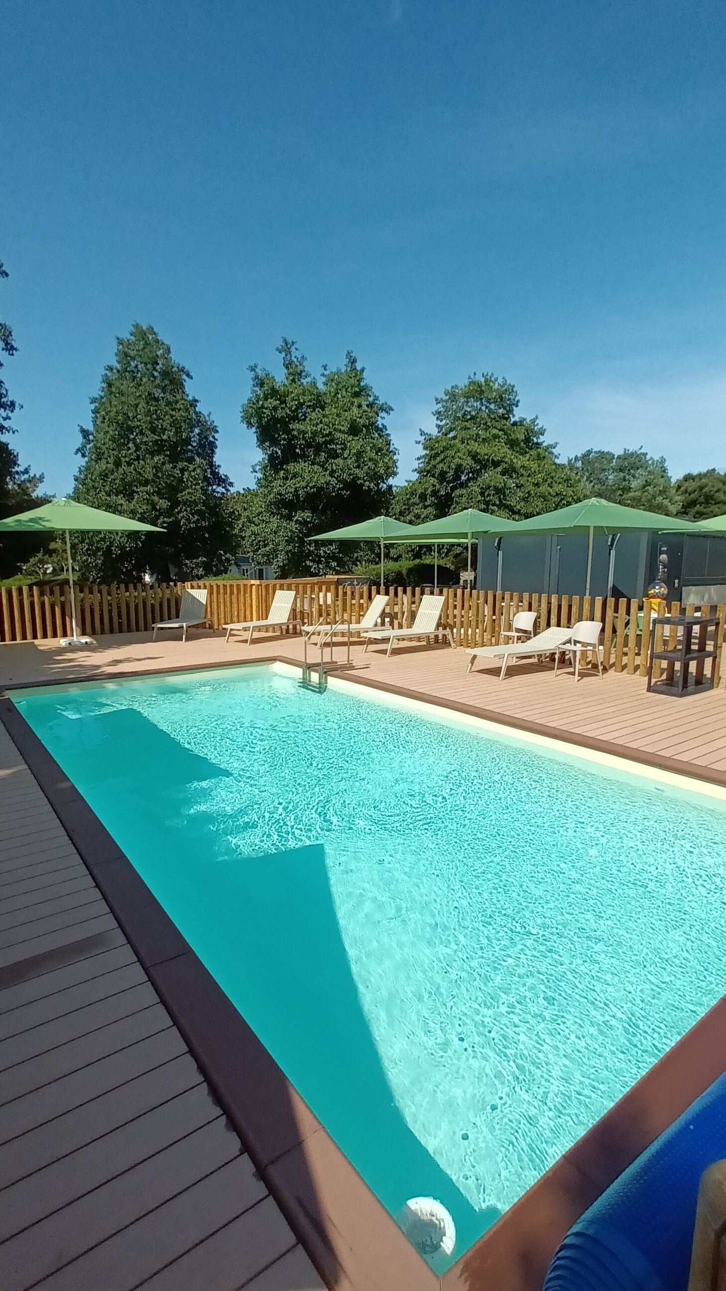 Una piscina rectangular amb una terrassa de fusta al voltant, equipada amb diverses gandules i paraigudes.