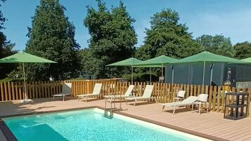 Una piscina rectangular amb una terrassa de fusta al voltant, equipada amb diverses gandules i paraigudes.