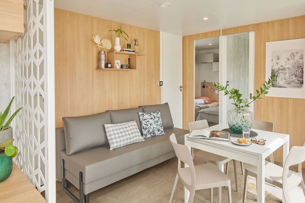 Ein modernes Wohnzimmer mit einem grauen Sofa, weißen Stühlen, einer Holzverkleidung und einem Esstisch mit einer Vase und Büchern.